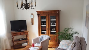A living room with a sofa, armchair, wooden cabinet, television, and a chandelier. - Vacation apartment Haus Junk am Lieserpfad (Daun)