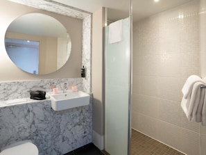 A bathroom with a marble sink, a round mirror, a glass shower enclosure, and a white towel hanging on the wall. - Ibis Styles Bordeaux Centre Gare (Bordeaux)