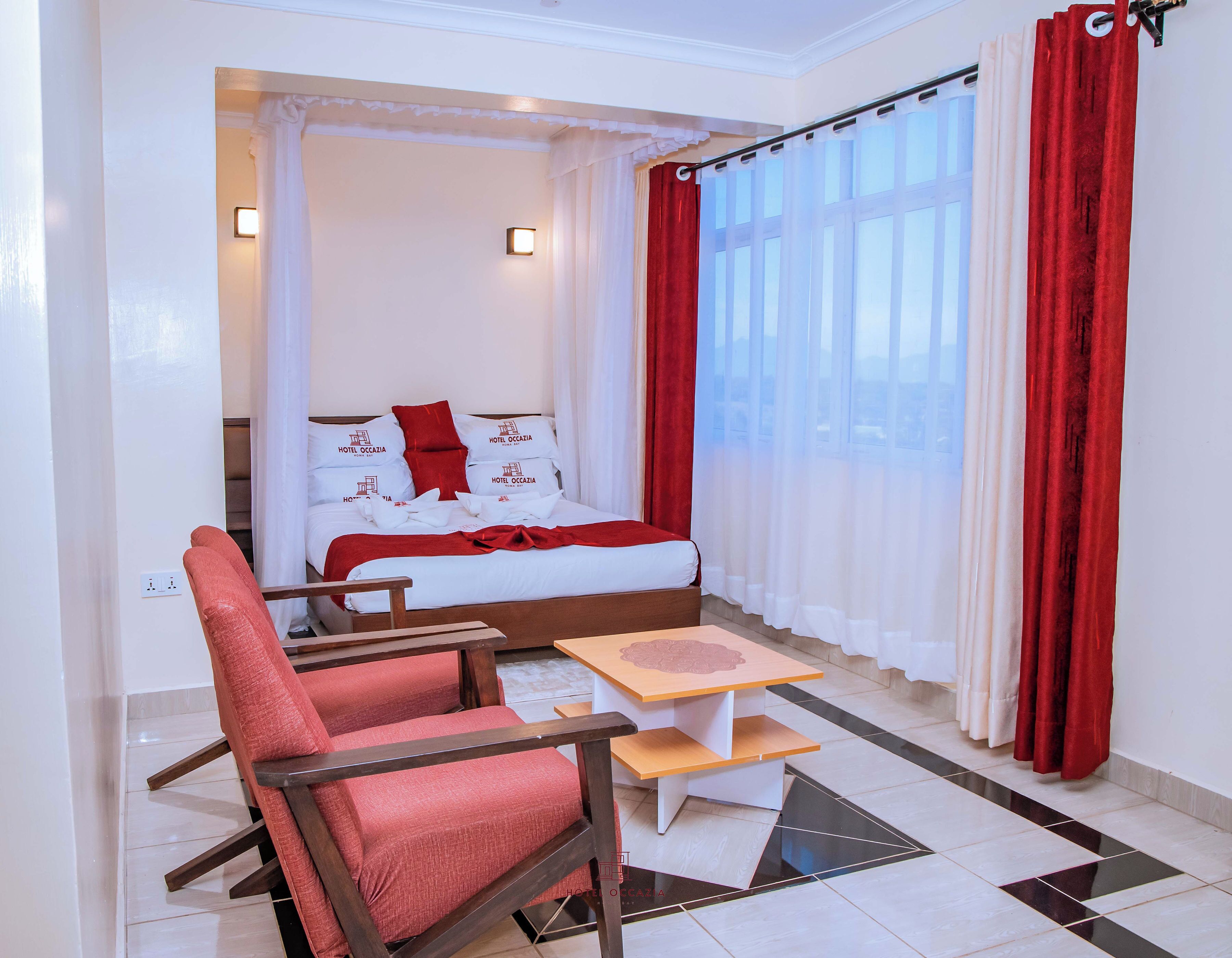 Una habitación de hotel con una cama, cortinas rojas y blancas, una mesita y una silla roja.