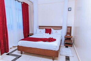 A hotel room with a wooden bed, white bedding, red accents, and a view of the outdoors. - Hotel OCCAZIA Homa Bay (Homa Bay)
