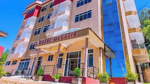 A multi-story hotel with a prominent sign reading "HOTEL OCCAZIA." It features balconies on each floor, large windows, and a red and beige facade. - Hotel OCCAZIA Homa Bay (Homa Bay)