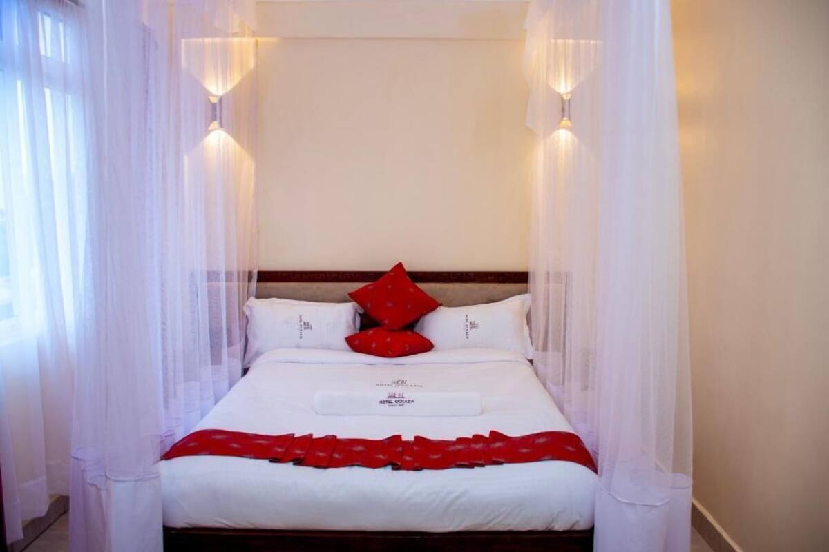 A hotel room with a bed, white bedding, red pillows, and a canopy.