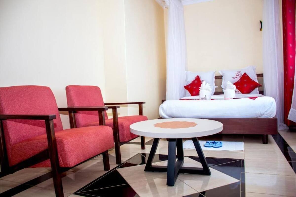 A hotel room with a bed, two red chairs, a small round table, and a white curtain.