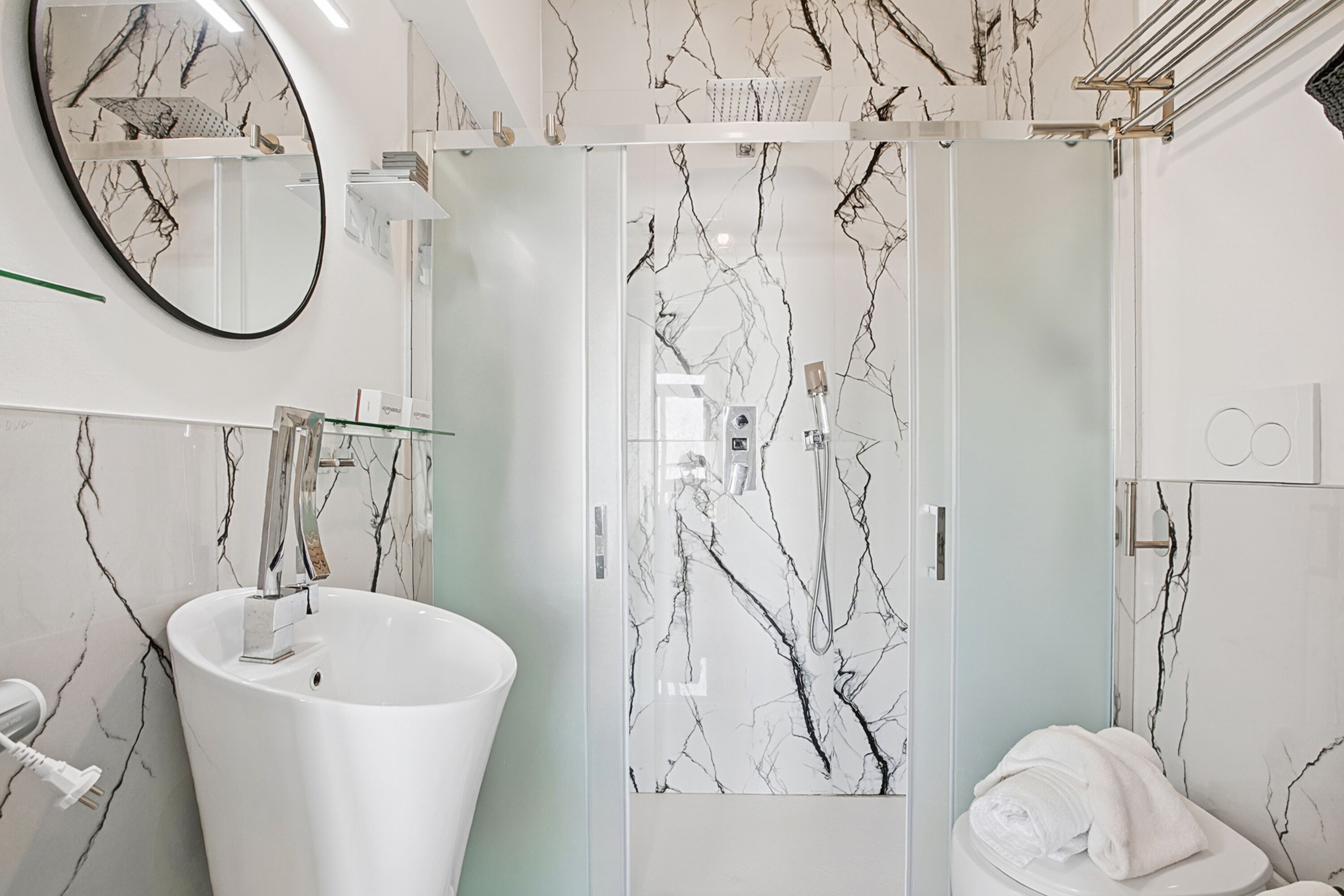 A bathroom with a white sink, a glass shower enclosure, a white toilet, and a mirror with a marble design.