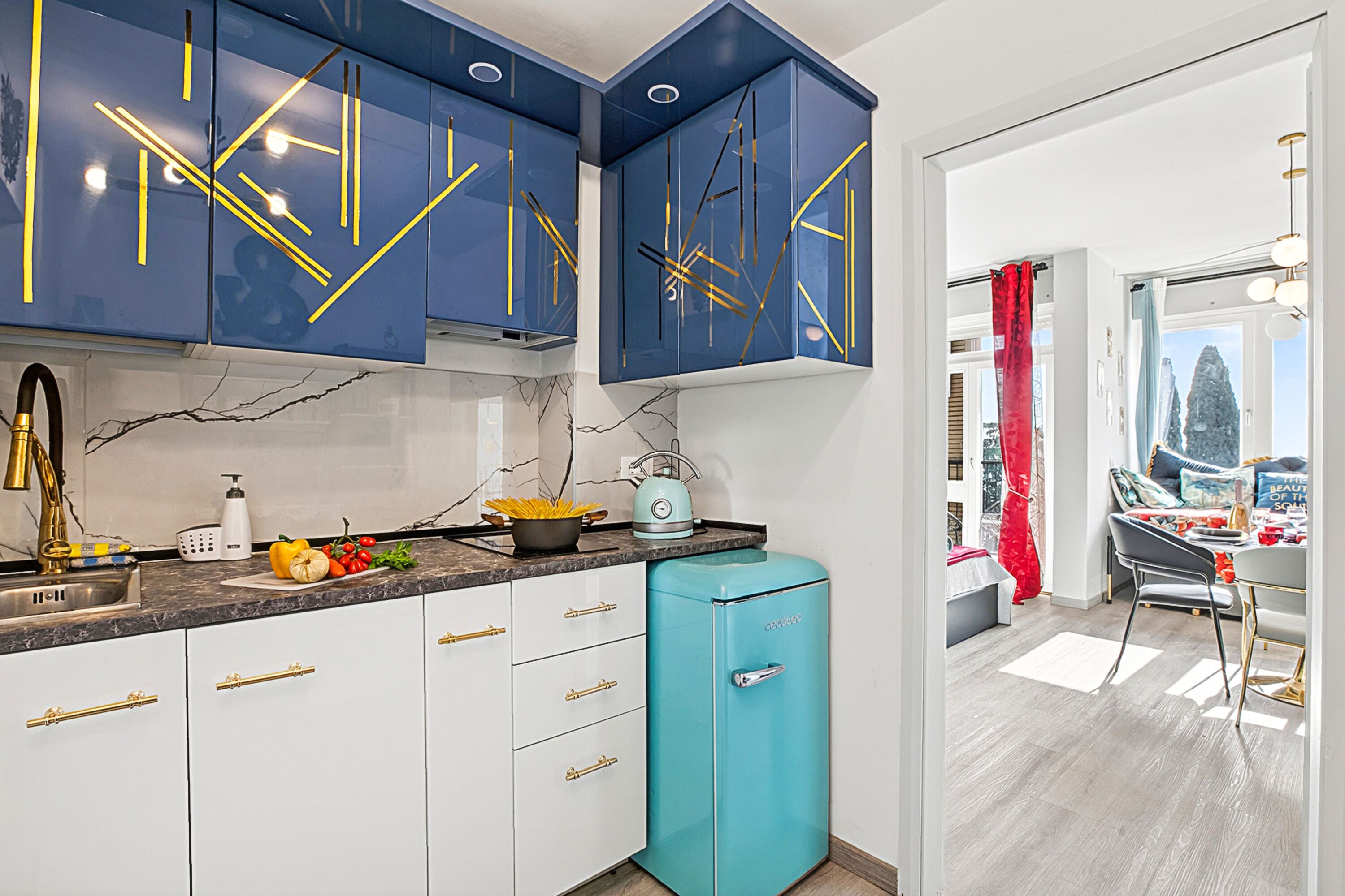 A kitchen with blue cabinets, a teal refrigerator, and a dining area with a table and chairs.