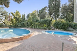 Un espace piscine comprenant deux piscines, entouré d’un sol en briques et de verdure.