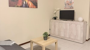 Een woonkamer met een bank, een salontafel, een televisie op een kast en kunstwerken aan de wanden.