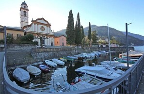 A marina with boats docked, a church with a bell tower, and a mountain in the background. - Bellagio San Giovanni Apartment (Bellagio)