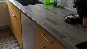 A kitchen with a wooden countertop, a dishwasher, a kettle, and a can of coffee.