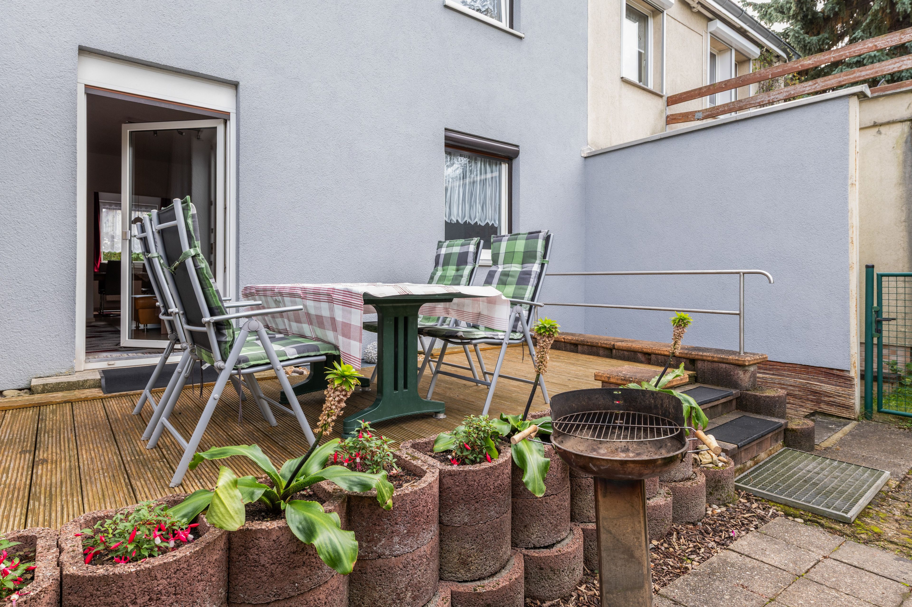 A patio with a table and chairs, a grill, and potted plants.