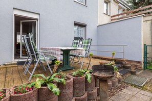 Eine Terrasse mit Tisch, Stühlen, einem Grill und Topfpflanzen.