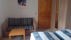 Une pièce avec un canapé à rayures, une table en bois et un lit recouvert d’une couvre-lit à motifs floraux.