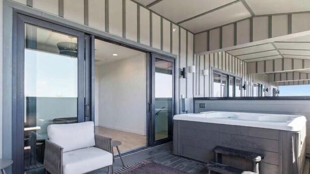 A modern interior with a sofa, a hot tub, and a glass door leading to an outdoor area. - 10BR Skyline Duo | Rooftop Hot Tub | Sleeps 28 (Nashville)