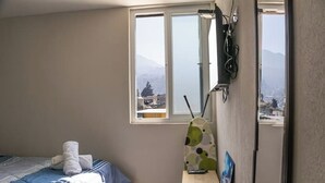 A bedroom with a bed, a window with a view of mountains, and a wall-mounted ironing board. - *comfortable loft in the center of Quetzaltenango (Quetzaltenango)