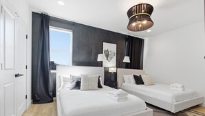 Quarto de hotel com duas camas, uma janela grande, um lustre e uma luminária na parede.