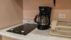 Una kitchenette con una cafetera negra, una jarra de vidrio y un escurreplatos.