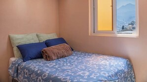 Un dormitorio con cama, almohadas y ventana con vista a la montaña.