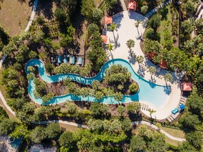 Vista aérea de un resort con piscina sinuosa, palmeras y tumbonas.