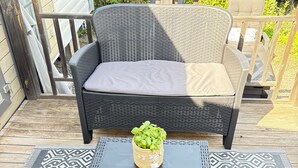 En fletsofà med puder på en udendørs terrasse, et lille bord med en vævet kurv og mønstrede tæpper.