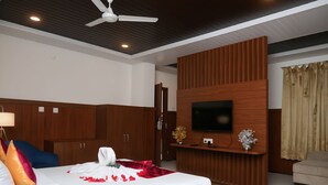 A modern bedroom with a wooden bed, a ceiling fan, a flat-screen TV, and a wooden wardrobe. - Hotel Orcella (Tirupati)