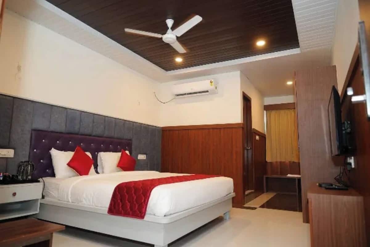 A modern hotel room with a large bed, a ceiling fan, an air conditioning unit, a wooden headboard, and a television on a wooden stand.