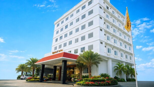 A multi-story hotel with a red and white facade, palm trees, and a flag. - Hotel Orcella (Tirupati)