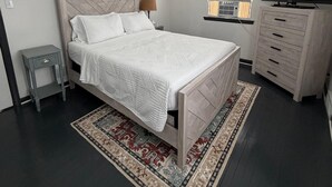 A modern bedroom with a bed, bedside table, dresser, and a TV. - Home Near Toll Road/BP/Hospitals 2 Bedroom (Gary)
