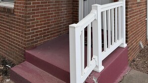 A brick house with a white door, a small porch with a white railing, and a mailbox on the wall. - Home Near Toll Road/BP/Hospitals 2 Bedroom (Gary)