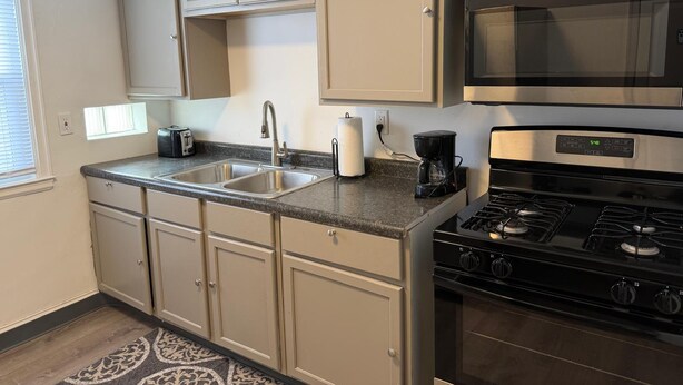 A kitchen with beige cabinets, a stainless steel sink, a coffee maker, a microwave, and a stove. - Home Near Toll Road/BP/Hospitals 2 Bedroom (Gary)