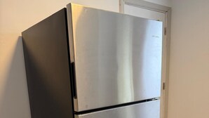 A stainless steel refrigerator in a room with wooden flooring and a white door in the background. - Home Near Toll Road/BP/Hospitals 2 Bedroom (Gary)