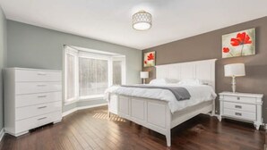 A bedroom with a large bed, a nightstand, a dresser, and a window with blinds. - Maple Nest Pickering for your stay (Pickering)