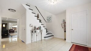 A spacious, well-lit hallway with a polished floor leading to a staircase with a white railing. - Maple Nest Pickering for your stay (Pickering)