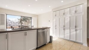 A modern kitchen with white cabinetry, a stainless steel dishwasher, and a large window offering a view of the outdoors. - Maple Nest Pickering for your stay (Pickering)