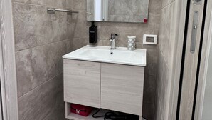 A bathroom with a white sink, a mirror, a towel dispenser, and a waste bin. - Domus Livia Vatican Cipro metro station (Roma)