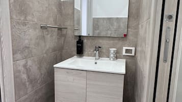 Une salle de bain avec un lavabo blanc, un miroir, un distributeur de serviettes et une poubelle.