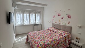 A bedroom with a bed, a TV, a window with curtains, and a wall with floral decals. - Domus Livia Vatican Cipro metro station (Roma)