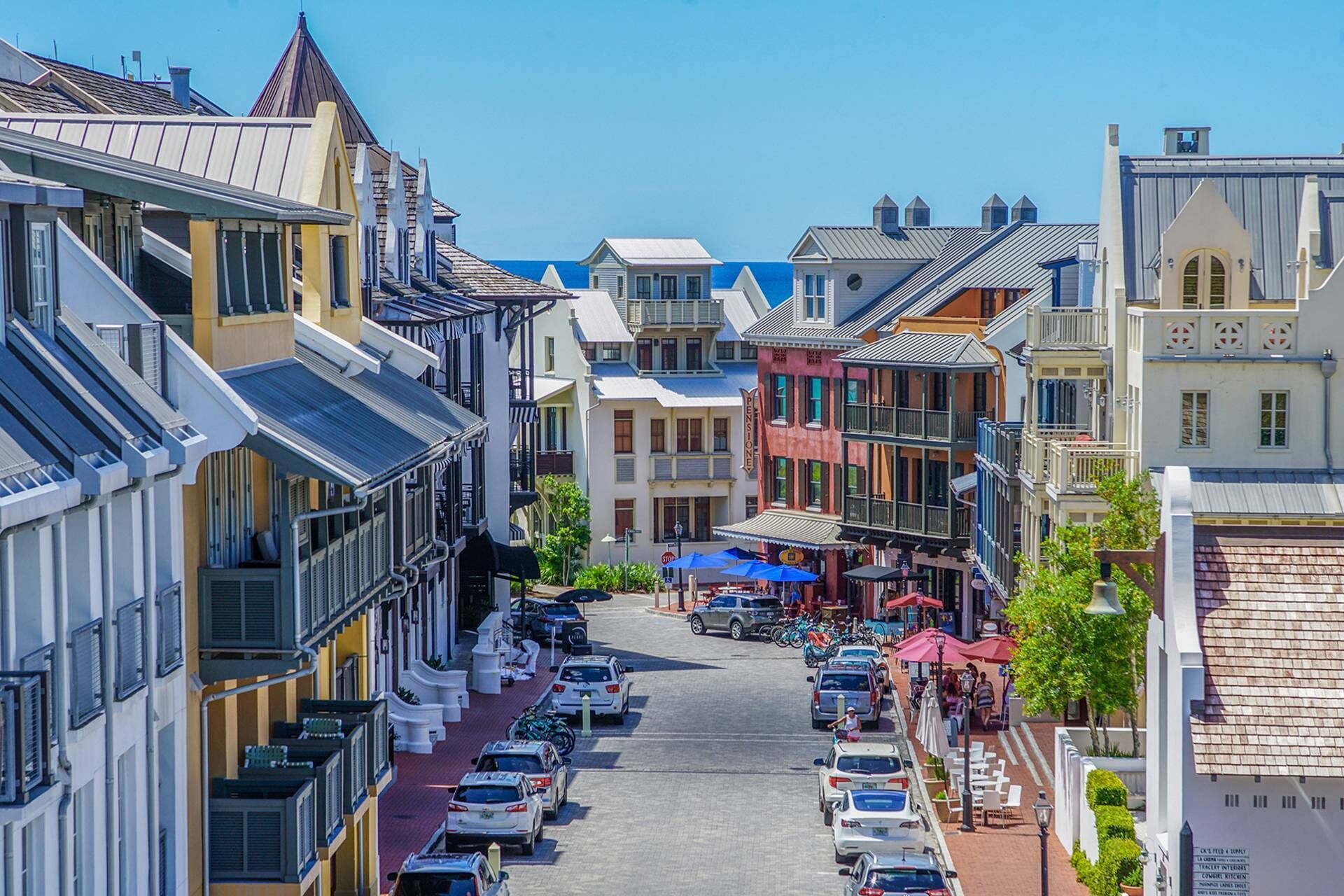 A street lined with historic buildings, parked cars, and outdoor seating areas.