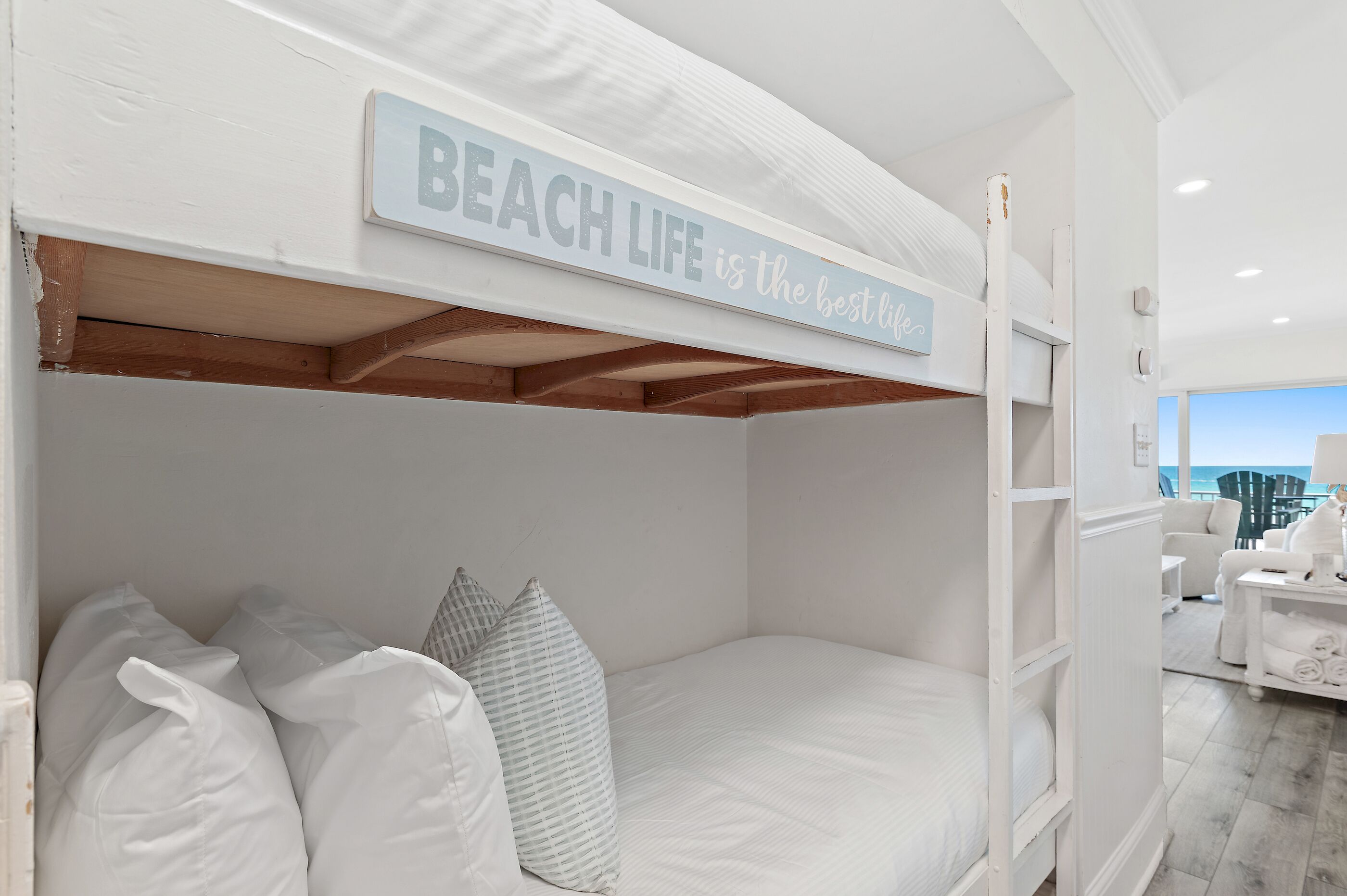 Un lit superposé avec une pancarte au-dessus indiquant : « LA VIE À LA PLAGE, c’est la meilleure des vies. »