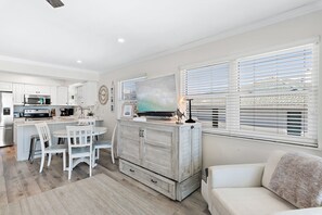 A modern kitchen with white cabinetry, a dining area with a round table and chairs, and a living area with a sofa and a TV. - Gulf Front Corner Unit - Seagrove Beach - Community Pool (Santa Rosa Beach)