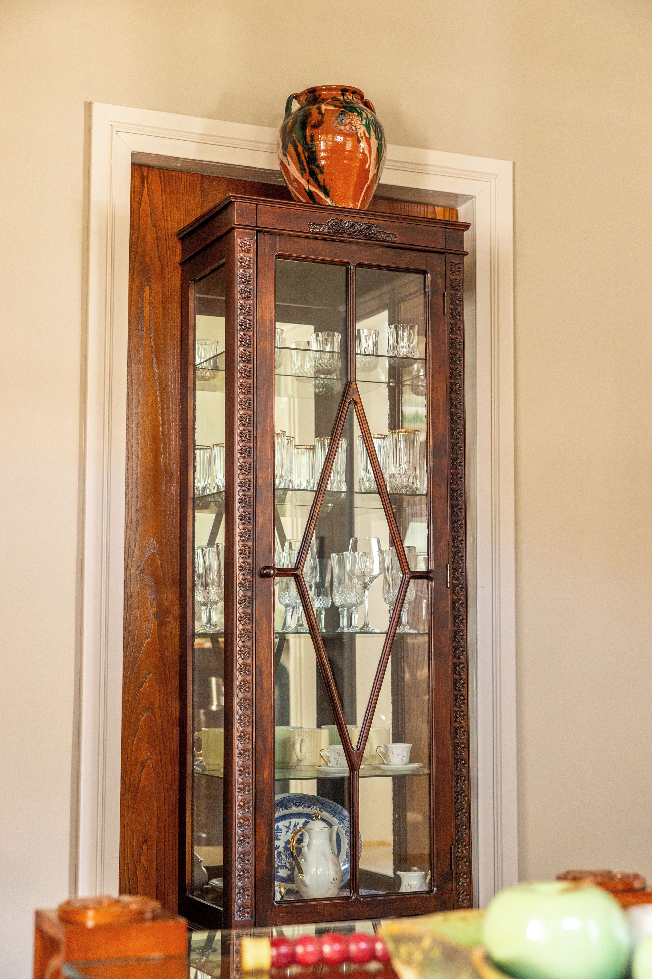 Een houten kast met glazen deuren, gevuld met divers servies en een decoratieve vaas erboven.