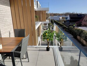 A balcony with a wooden table and chairs, potted lemon trees, and a view of the surrounding buildings. - Luxury Apartment With Pool & Parking (Nieuwpoort)