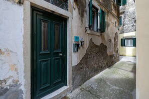 Un estrecho callejón con una puerta verde, una pared desgastada y un pequeño ventanal con contraventanas.