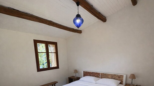 A bedroom with a large bed, wooden beams, a window, and a hanging light fixture. - Villa Carla in Bastia – Sleeps 5 – Bright & peaceful home – Terrace & garden (Bastia)