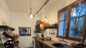 A modern kitchen with wooden cabinets, a built-in oven, a dishwasher, and a window with a view of trees. - Villa Carla in Bastia – Sleeps 5 – Bright & peaceful home – Terrace & garden (Bastia)