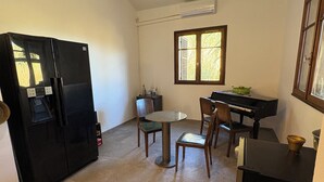A compact kitchen with a built-in refrigerator, a dining table with chairs, a window with blinds, and a small black cabinet. - Villa Carla in Bastia – Sleeps 5 – Bright & peaceful home – Terrace & garden (Bastia)