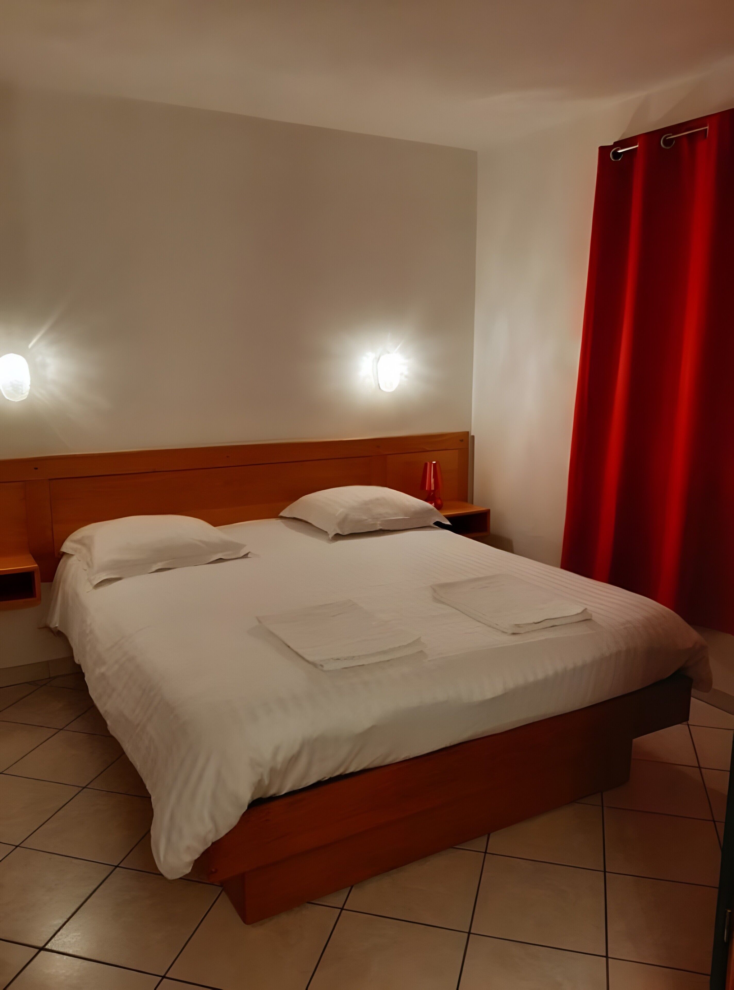 Ein ordentlich bezogenes Bett mit weißen Leinen, zwei Nachttische mit Lampen und ein roter Vorhang am Fenster.