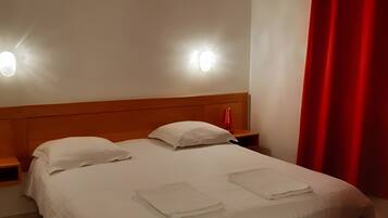 Ein ordentlich bezogenes Bett mit weißen Leinen, zwei Nachttische mit Lampen und ein roter Vorhang am Fenster.