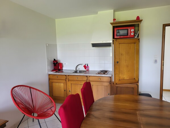 A kitchen with wooden cabinets, a microwave, a sink, and a dining area with a wooden table and red chairs.