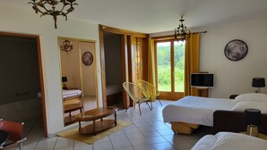 Ein Hotelzimmer mit zwei Betten, einem Fernseher, einem Sessel und einem großen Fenster mit Vorhängen.