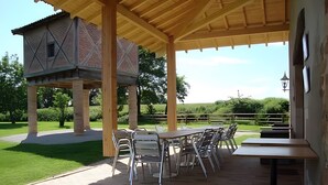 Eine überdachte Terrasse mit Gartenmöbeln, ein Backsteinhaus und Blick ins umliegende Grün.